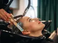 Profesjonalna pielęgnacja włosów farbowanych w salonie. Stylistka nakłada maskę na mokre włosy klientki.