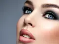 Niebieskie oczy z perfekcyjnym makijażem smokey eye, podkreślone długimi rzęsami i błyszczącymi ustami.