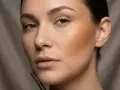 Modelka z ciemnobeżowym bronzerem na policzku, który nadaje jej ciepły, słoneczny wygląd.