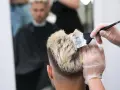 Fryzjer nakłada farbę na blond włosy mężczyzny.