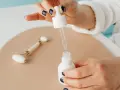 Dłoń z ciemnym lakierem do paznokci aplikuje serum z pipety do białej buteleczki. Obok leży jadeitowy roller. Zastanawiasz się, z czym łączyć niacynamid?