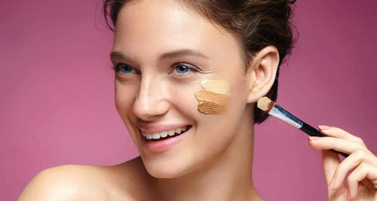 Uśmiechnięta kobieta testuje odcienie podkładu na policzku. Elektroniczne dobieranie podkładu ułatwia znalezienie idealnego koloru.