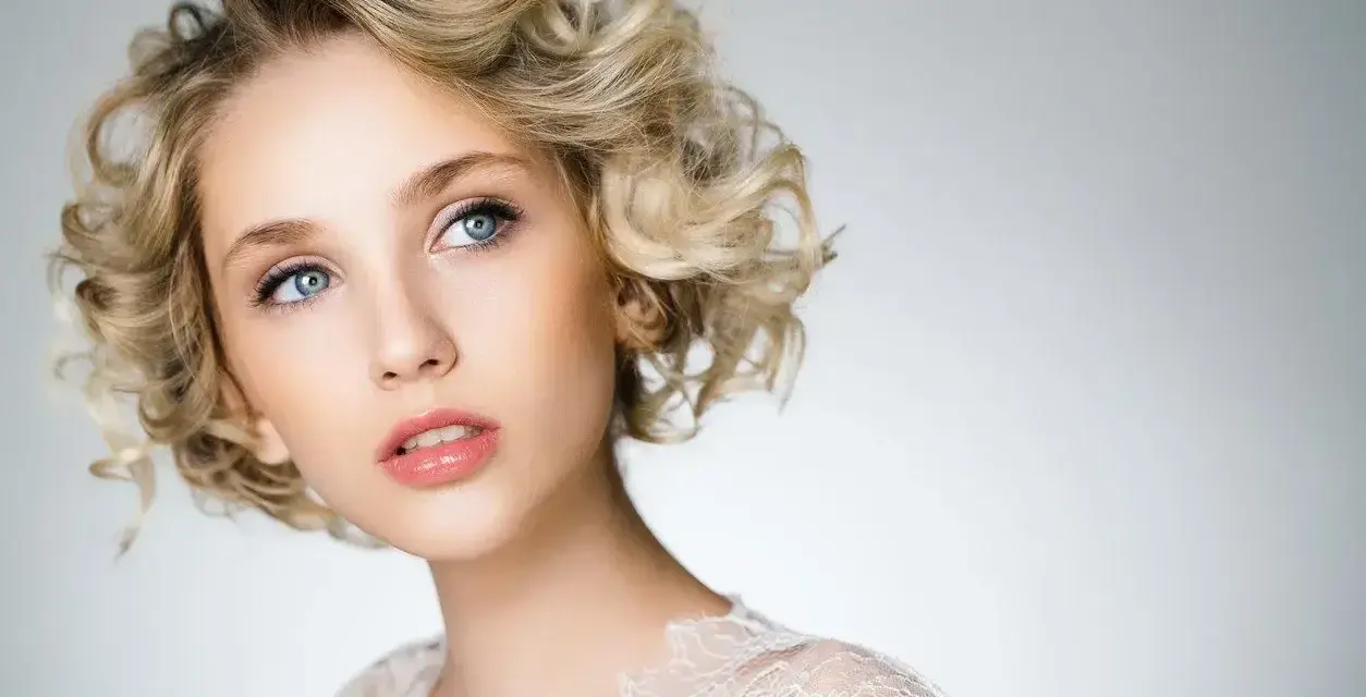 Blondynka z błękitnymi oczami i kręconymi włosami, prezentująca subtelny makijaż smoky eyes.