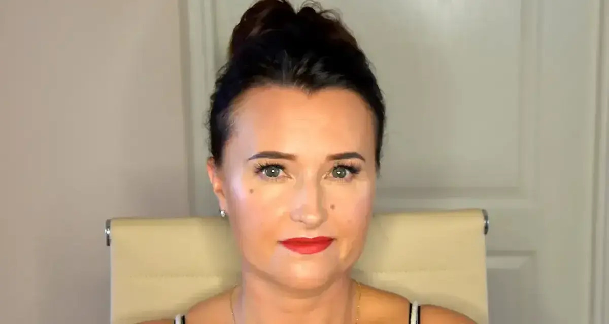 Kobieta z upiętymi włosami prezentuje perfekcyjny makijaż wieczorowy. Czerwone usta i podkreślone oczy dodają jej uroku.