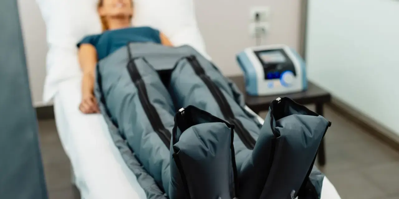 Kobieta leży na łóżku, jej nogi są w specjalnych mankietach. To presoterapia, zabieg poprawiający krążenie i redukujący obrzęki.