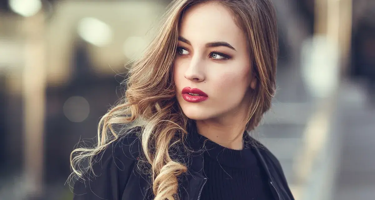 Blondynka z burzą falowanych włosów i wyrazistymi, czerwonymi ustami. Idealny kolor pomadki dla blondynek podkreśla jej urodę.