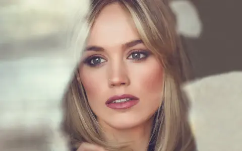 Kobieta z blond włosami i wysokim czołem, patrząca w bok z zamyśleniem.