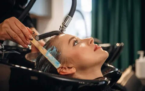 Profesjonalna pielęgnacja włosów farbowanych w salonie. Stylistka nakłada maskę na mokre włosy klientki.