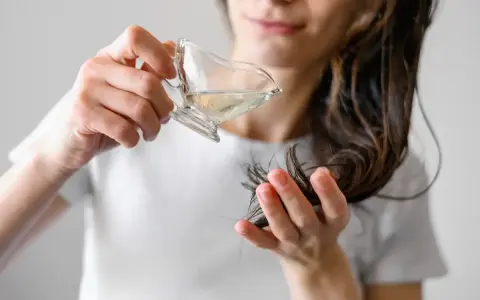 Kobieta aplikuje hydrolat do włosów, przelewając go z małego naczynia na pasma włosów.