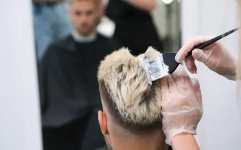 Fryzjer nakłada farbę na blond włosy mężczyzny.