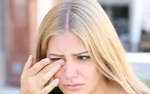 Kobieta z blond włosami pociera oko, co może być jednym z objawów niedoboru witaminy B.