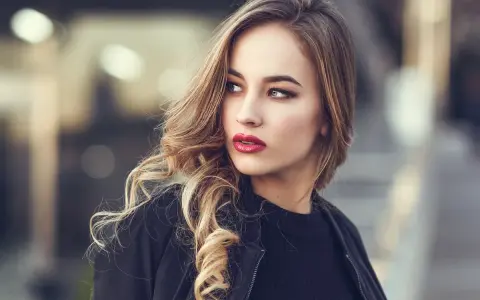 Blondynka z burzą falowanych włosów i wyrazistymi, czerwonymi ustami. Idealny kolor pomadki dla blondynek podkreśla jej urodę.