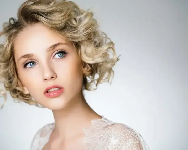 Blondynka z błękitnymi oczami i kręconymi włosami, prezentująca subtelny makijaż smoky eyes.