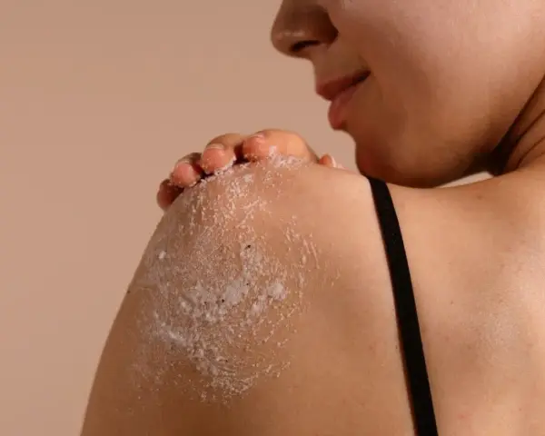 Kobieta wykonuje peeling całego ciała, delikatnie masując ramię.