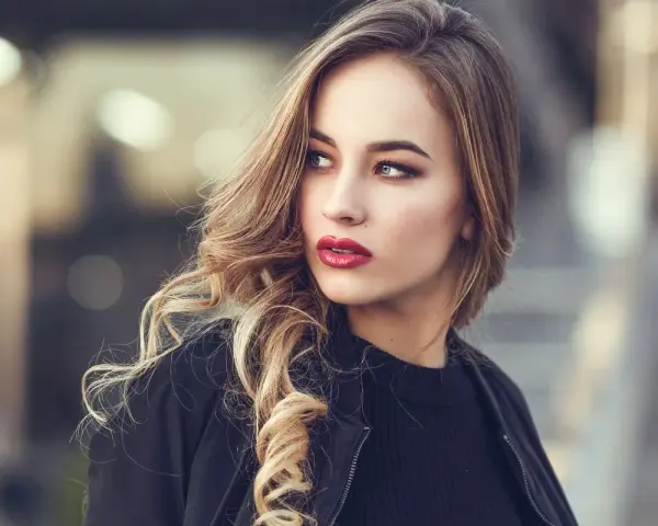 Blondynka z burzą falowanych włosów i wyrazistymi, czerwonymi ustami. Idealny kolor pomadki dla blondynek podkreśla jej urodę.