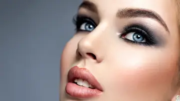 Niebieskie oczy z perfekcyjnym makijażem smokey eye, podkreślone długimi rzęsami i błyszczącymi ustami.